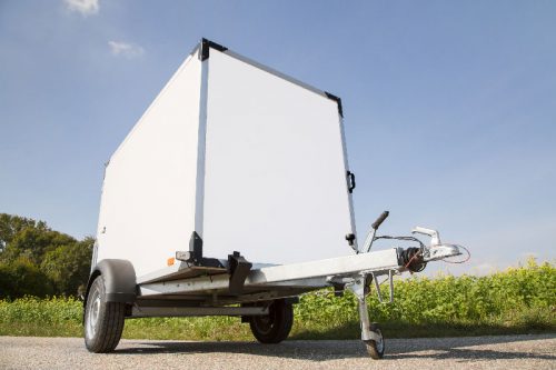 Kofferanhänger steht vor einer Wiese auf einem Weg